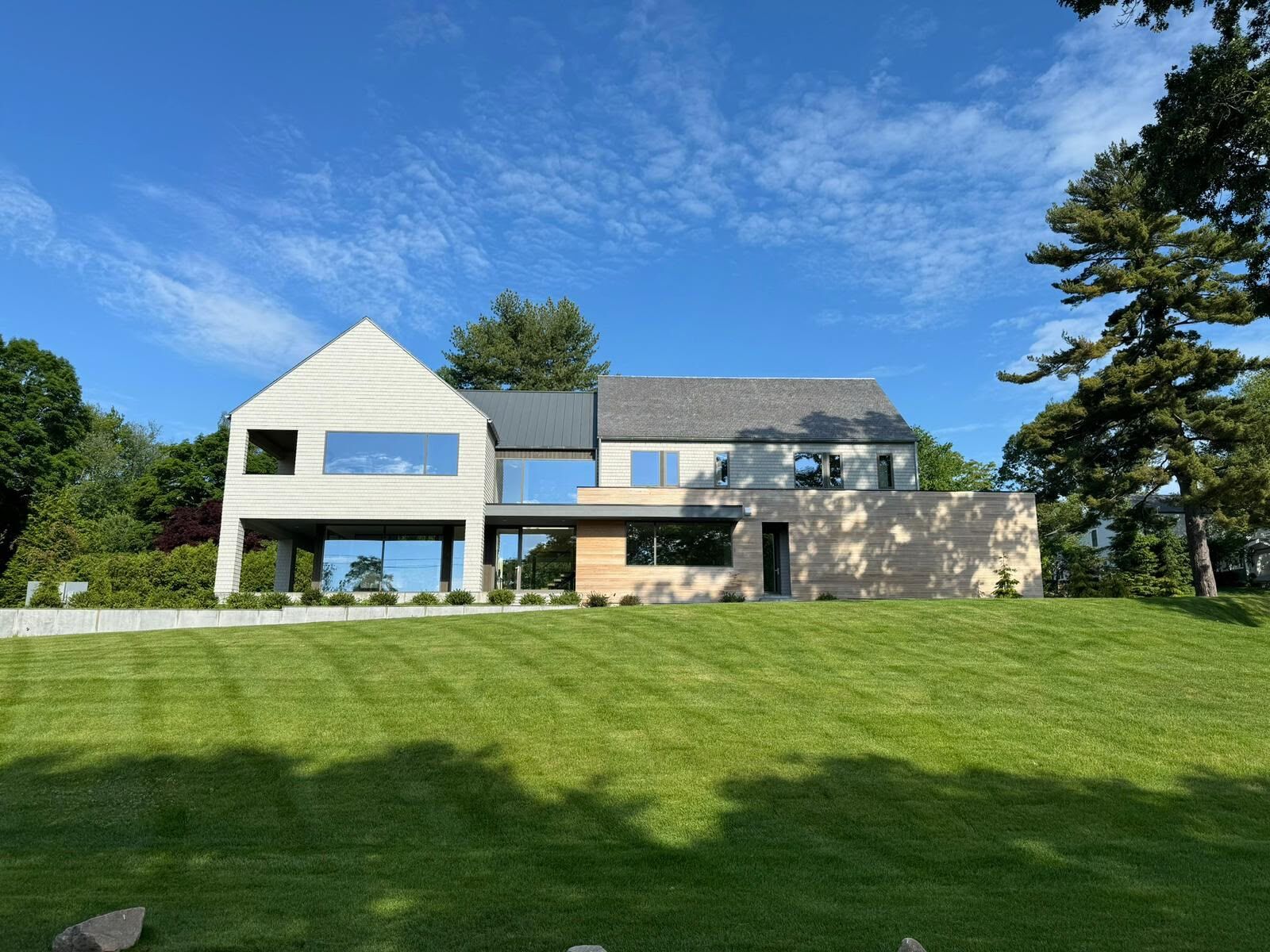 Light-colored modern home with large window openings above a green lawn